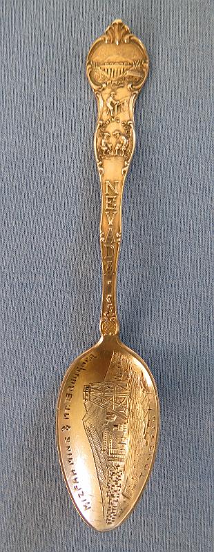 Souvenir Mining Spoon Mizpah Mine Tonopah NV.JPG - SOUVENIR MINING SPOON MIZPAH MINE TONOPAH NV - Sterling silver souvenir demitasse spoon, features handle with miners and marked NEVADA, bowl withdetailed engraving of Mizpah mine scene and marked MIZPAH MINE & MT. BROUGHER at top and TONOPAH across bottom, length 4 1/8 in., marked on reverse Sterling and maker’s mark of S in a circle for Shepard Mfg. Co. MelroseHighlands, MA 1893-1923 (Mt. Brougher is a 6,500 ft. summit just to the west of Tonopah town) [Tonopah is an unincorporated town and the county seat of Nye County, Nevada. It is located approximately midway between Las Vegas and Reno.  One of the richest booms in the west occurred at Tonopah Springs on May 19, 1900. And the name Jim Butler will forever be associated with the name Tonopah and the many stories that surround the discovery. The legendary tale of discovery says that he went looking for a burro that had wandered off during the night and sought shelter near a rock outcropping. When Butler discovered the animal the next morning, he picked up a rock to throw at it in frustration, noticing that the rock was unusually heavy. He had stumbled upon the second-richest silver strike in Nevada history. News of the discovery traveled to the Klondike and soon scores of eager prospectors were searching the area. But it was not until August 27, 1900 that Butler and his wife filed on eight claims near the springs, six of which were some of the biggest producers the state has ever had including the Desert Queen, Burro, Valley View, Silver Top, Buckboard, and Mizpah, the largest silver producer in the district. Because the Butler claims were known far and wide, the town was often referred to as Butler. By the summer of 1901, the mines around the town produced nearly $750,000 worth of gold and silver. Now it was time for a post office and one opened on April 10, 1901 named Butler.  By 1902 Jim Butler had sold his claims, which were all consolidated and gave birth to a new company, the Tonopah Mining Company. It was incorporated in Delaware, with stock listed on both the Philadelphia and San Francisco exchanges. The company, with J.H. Whiteman as president, controlled 160 acres of mineral-bearing ground around the Tonopah district. The company also had holdings in the Tonopah-Goldfield Railroad and controlled mining companies in Colorado, Canada, California and Nicaragua. The mine workings at Tonopah consisted of three deep shafts with more than 46 miles of lateral workings. The deepest of the three shafts was 1,500 ft. The ore mined at the site was treated in a 100-stamp mill. Also in 1902 the Tonopah-Belmont Mining Company was formed and was based in New Jersey with C.A. Heller as president. The company’s property, 11 claims covering more than 160 acres, was on the east side of the property owned by the Tonopah Mining Company. There were two deep vertical shafts, 1,200 and 1,700 ft, with workings covering almost 39 miles.  Butler now had a population of 650 and was increasing every day. It also had six saloons, restaurants, assay offices, lodging houses, and a number of doctors and lawyers. It was not until March 3, 1905 that its name was changed to Tonopah. By 1907, Tonopah had become a full-fledged city with modern hotels, electric and water companies, five banks, schools, and hundreds of other buildings. Tonopah’s mines continued to produce extremely well until the Depression brought a slowdown. From 1900 to 1921, they produced ore worth almost $121 million. Tonopah’s biggest year was 1913 when its mines yielded almost $10 million worth of gold, silver, copper, and lead. By the time World War II started, only four major mining companies were operating in Tonopah. At the end of the war even the companies that had been there at the beginning were gone. In 1968, Howard Hughes and his Summa Corporation bought 100 claims in Tonopah, including the Mizpah, Silver Top, and Desert Queen mines. Hopes for a mining revival soon faded after disappointing core samples were taken. A few of the old mines were re-timbered but never reopened. The value of the Tonopah district’s total production is just over $150 million.  Today tourism plays a large part in the local economy.]